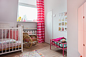 Gitterbett, Schaukelstuhl vor Fenster mit pinkem Vorhang und Puppenbett im Mädchenzimmer