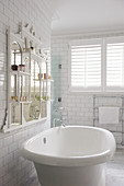 Free-standing bathtub below mirror with integrated shelves on wall