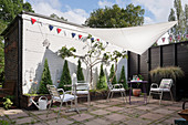 Metal chairs and tables on paved terrace with bunting and awning