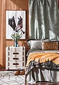 Bedside table with a suitcase look, picture with horse motif above, bed with gray bedclothes in the bedroom