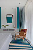 White bedroom with turquoise accents and chair next to window with floor-length curtains