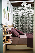 Double bed with bed linen in berry shades, grey-green wallpaper and mobile