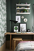 Desk, stool and shelves against green wall in bedroom
