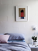 Bed and bedside table in front of white wall with picture in bedroom