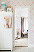 White wardrobe with girl's dress hung from door and view of dolls' pram in nursery