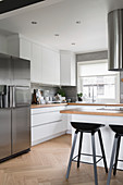 White fitted kitchen with stainless steel fridge, island counter and bar stools