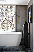 Free-standing bathtub below window decorated with branches