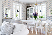 White dining table and chairs in open-plan interior with blue-and-white wallpaper
