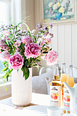 Vase of peonies and selection of juices on kitchen table