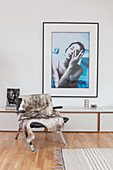 Fur blanket on leather armchair in front of console table below photographic artwork