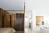 Sliding wooden screens around sleeping area with white designer sofa and dining area in background
