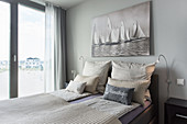 Bedroom in pale shades with maritime artwork above bed and view of beach