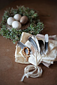 Feathers and cross on wooden beads on white cloth in front of speckled eggs on pewter plate in Easter nest