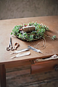 Handmade chickweed Easter nest with twine, wooden beads, scissors and feathers on wooden table