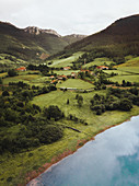 Einzelne Häuser auf grünen Feldern zwischen Bergen und Gewässer