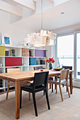 Designer lamp above dining table in front of shelving with colourful compartment doors