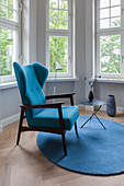 Blue wing-back chair and side table on round rug in window bay