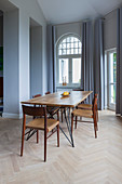 Dining table with wooden top and chairs in front of arched window in period apartment