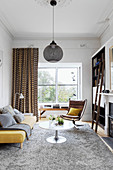 Gelbes Polstersofa, Coffeetable und Klassikerstuhl im Wohnzimmer mit grauem Teppich