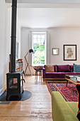 Log-burning stove and sofas in purple velvet and lime-green upholstery in living room