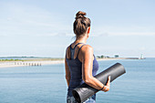 Woman holding yoga mat next to the sea