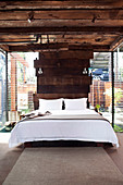Bett vor Wand aus Holzbohlen im Schlafzimmer mit Lamellenfenstern