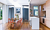 Esstisch mit orangefarbenen Stühlen vor offener Küche mit Theke