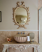 Ornate mirror and shell-shaped sink on antique console table in bathroom