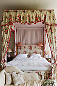 Four-poster bed with chintz curtains in bedroom in English manor house