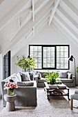 Bright living room under white gable roof with grey sofas and black mullioned windows