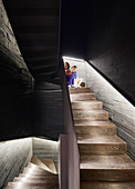 Two children in dark stairwell with board-formed concrete walls