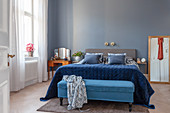 Bett mit blauem Samtüberwurf und Bettbank im Schlafzimmer einer Altbauwohnung