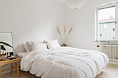Doppelbett mit weißer Bettwäsche in weißem Schlafzimmer