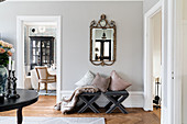 Cushions on upholstered stools below antique mirror on wall and view into dining room