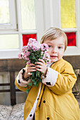 Boy wearing yellow jacket holding bunch of flowers