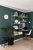String shelves with desk top and houseplants in room with green walls