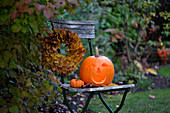 Halloween pumpkin and wreath of sycamore leaves on garden chair