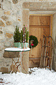 Gartentisch mit Tannenbäumchen vorm Natursteinhaus mit Holztür