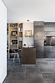 Breakfast bar used as partition between floor-to-ceiling shelving and concrete-effect kitchen