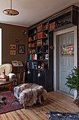 Floor-to-ceiling bookcase in dark wood, antique sofa and fur blanket on ottoman