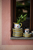 Stacked plates and jug with branch of bay leaves on windowsill