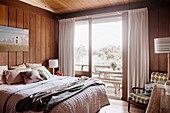 Schlafzimmer mit Holzwänden und breiten Schiebetüren zum Balkon