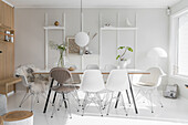 Dining table and various Eames chairs in white interior with wooden elements