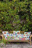 Colourful cushions on garden bench in front of lemon tree against wall