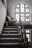 Carpet on staircase with armchair on landing with arched window in old factory