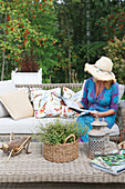 Woman wearing sunhat sitting on sofa on terrace with woods in background