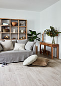 Sofa with grey loose cover and scatter cushions in front of wooden shelving in living room