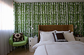 Double bed with rattan headboard, bedside cabinets and green armchair against green-and-white curtain in bedroom
