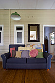 Collection of scatter cushions on sofa and mirror on wood-clad wall in living room