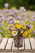 Posy of dyers' chamomile, ox-eye daisies and scabious on wooden chair in field of purple tansy